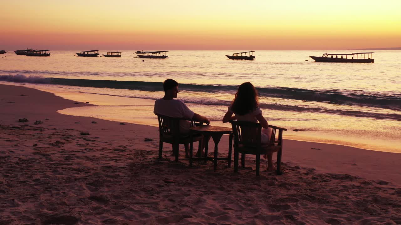 Young man and woman sitting in chairs and watching the beautiful orange sunset on a beach resort