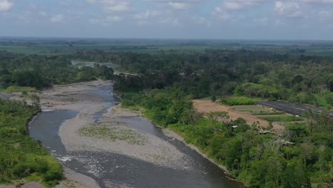 Overview-of-industrial-lots-and-farms-near-low-level-river-affected-by-drought-in-San-Jose,-Costa-Rica,-Aerial-pan-left-reveal-shot