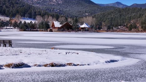 Frozen-ice-Evergreen-Lake-House-aerial-cinematic-drone-hockey-player-ice-skater-dream-fresh-first-snow-freezing-ice-winter-cold-bluebird-sunny-noon-downtown-golf-course-pan-up-forward-movement