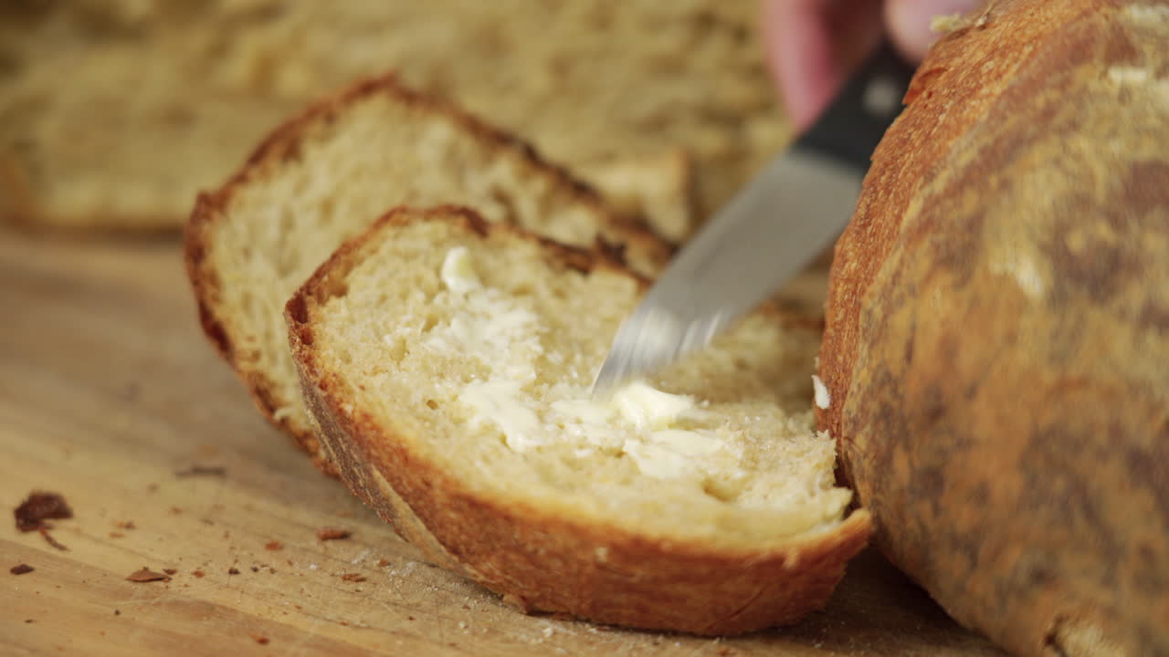Baker spreading some butter on a crusty sourdough bread