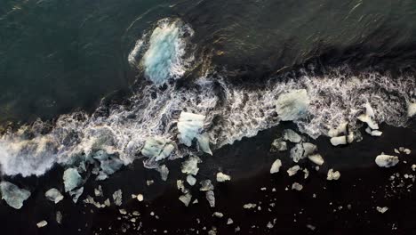 aerial top down shot of waves reaching shore and beach with icebergs of diamond beach, iceland