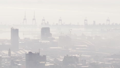 general view of cityscape with multiple buildings and shipyard covered in fog