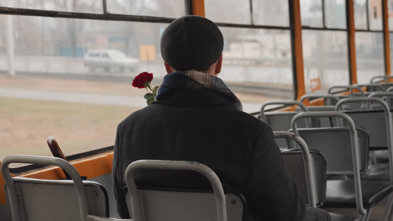 Creatore nero su tram che tiene una rosa, pendolare contemplativo diventato poeta e messaggero romantico attraverso sedili vintage vuoti con vista da finestra nuvolosa, sciarpa e berretto, illuminazione cinematografica morbida, intima