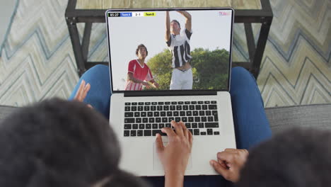 Hands-using-laptop-with-diverse-male-soccer-players-playing-match-on-screen