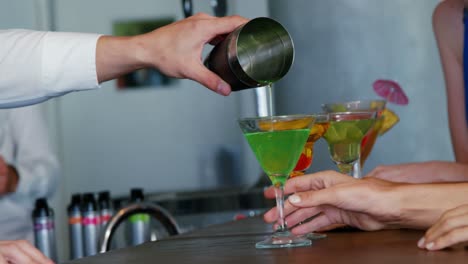 bartender pouring cocktail from a shaker at bar counter for customer