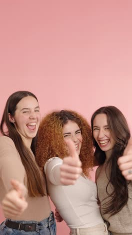 young women showing thumbs up on pink background