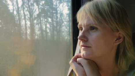 Portrait-Of-A-Young-Woman-Traveling-In-A-Train-Looking-Out-The-Window-The-Sun's-Rays-Illuminate-Her-