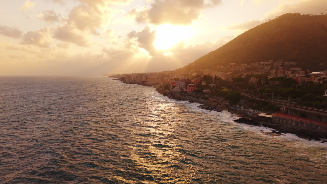 Peaceful drone view of golden sunset over Mediterranean coastal town with waves hitting rocky shore
