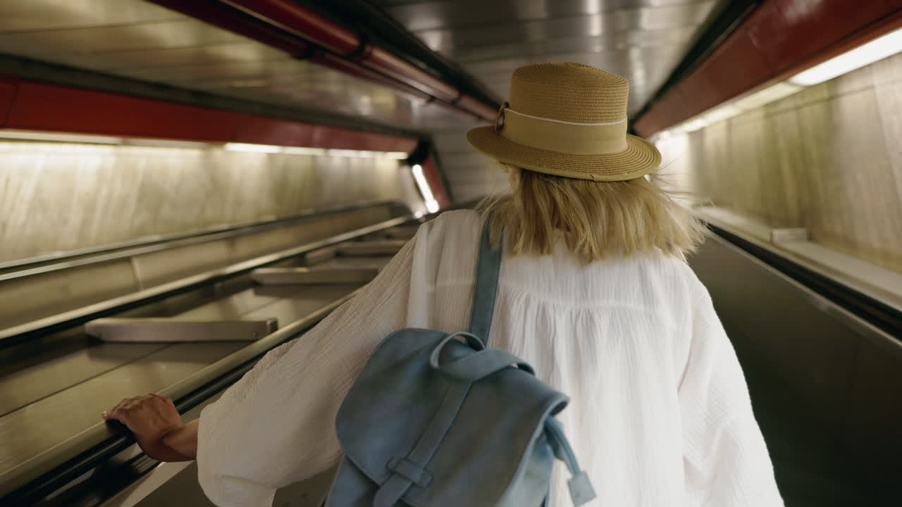 Woman on Escalator with Backpack and Hat
