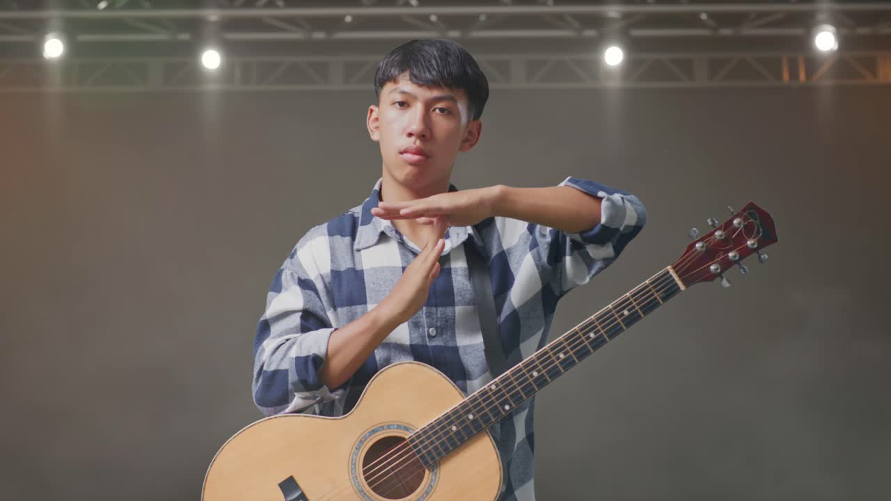 adolescente asiático con guitarra haciendo un gesto de tiempo con las manos en el escenario