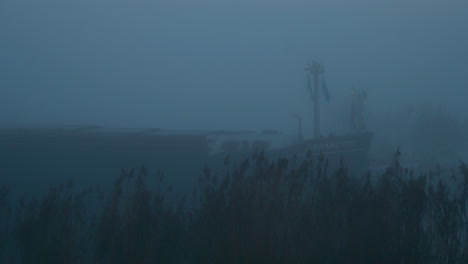 bulk carrier ship sailing in the mysterious morning fog, across the ferry bay of genemuiden, netherlands