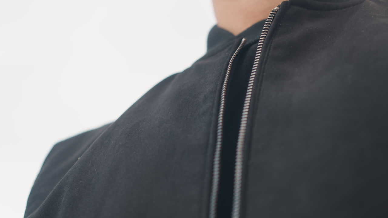 Hombre arreglándose la chaqueta en el exterior, modelo masculino ajustándose la chaqueta en un entorno urbano al aire libre con el horizonte de la ciudad al fondo, hombre con una chaqueta negra estilo bomber ajustándola cerca de la cremallera en medio del paisaje urbano