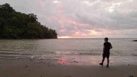 young caucasian man walking to an empty beach with a magnificent cloudy sunset on the horizon