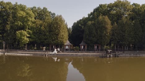 a bride and groom walking along a lake with trees in the background