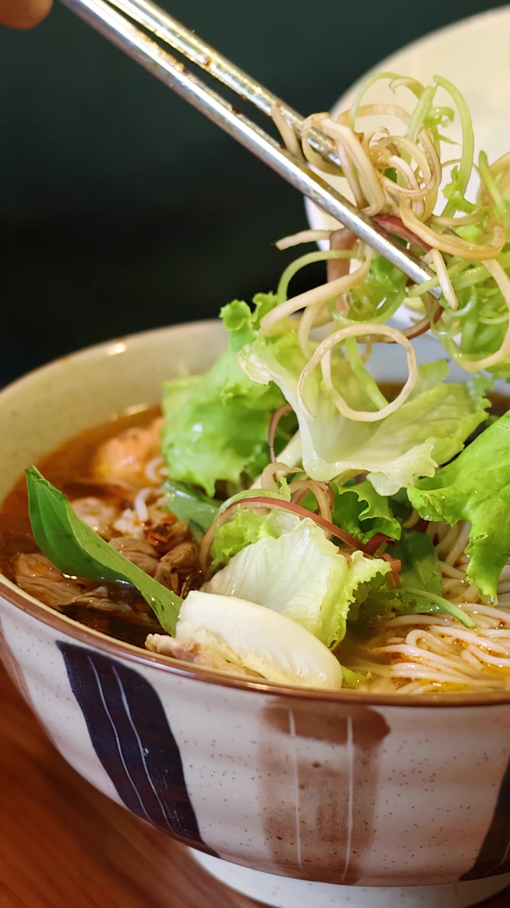 Primo piano di mani che usano le bacchette per aggiungere verdure fresche in una ciotola di ceramica per noodle