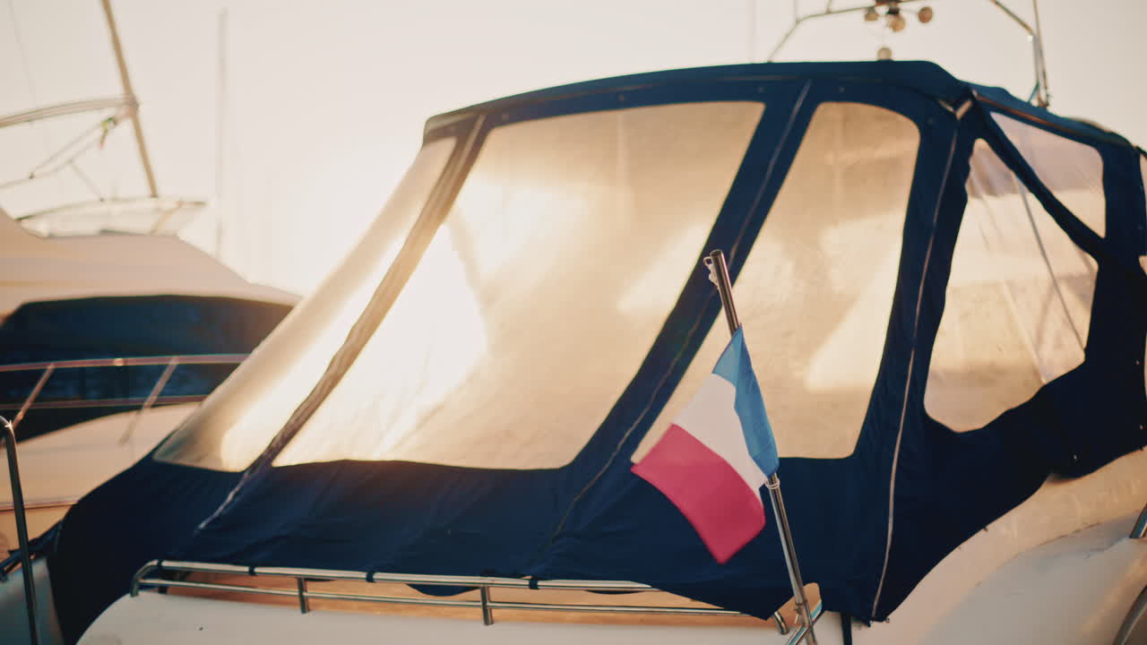 A French flag waves gently beside a sunlit boat canopy in a marina during early morning light
