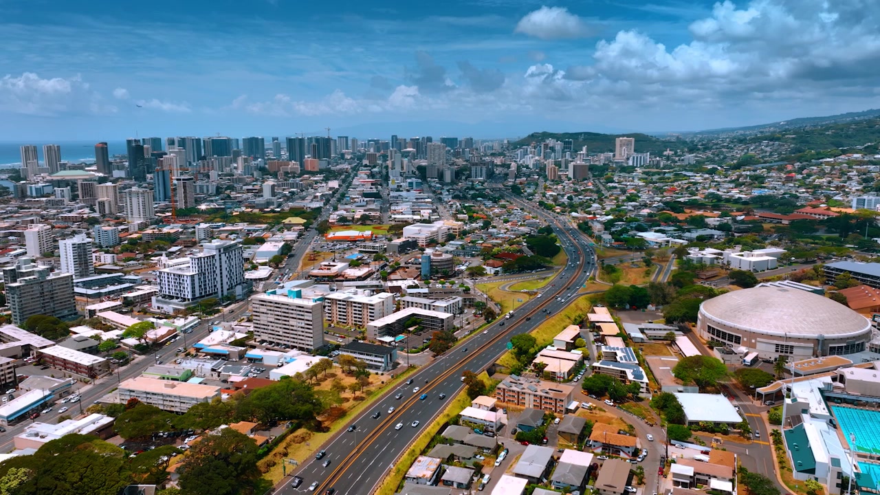 Auto che sfrecciano lungo le autostrade che attraversano il paesaggio della moderna Honolulu, Hawaii, USA. Prospettiva aerea sulla splendida città in una giornata soleggiata ma nuvolosa