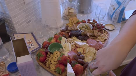 woman filling a charcuterie board in a brightly lit kitchen