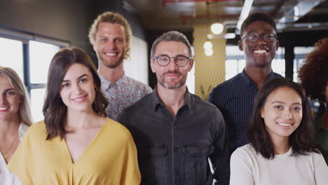 Creative-team-standing-together,-looking-to-camera-in-their-office,-waist-up