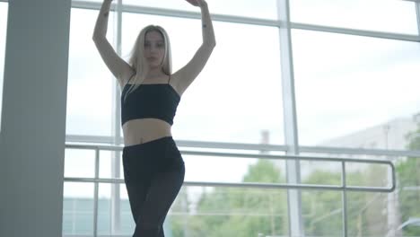 fit girl in black clothes performing contemporary. female dancer shows flowing motions, body and hands waves at white room. modern ballet dance choreography. young woman is moving smoothly