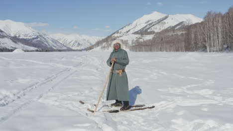 tuva man standing in snow with traditional clothing and ancient fur skis smiling at camera. winter day