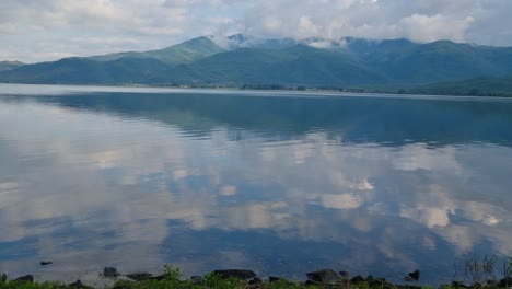 view of kerkini reservoir lake in northern greece on a cold spring day, with surrounding mountains and cloudy sky mirrored in the calm, clear water