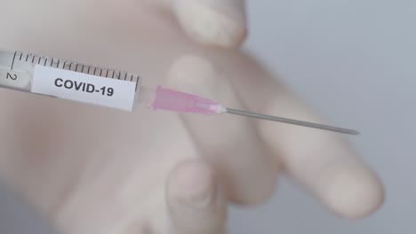 hand with glove flick off the syringe with covid 19 vaccine, close up shot