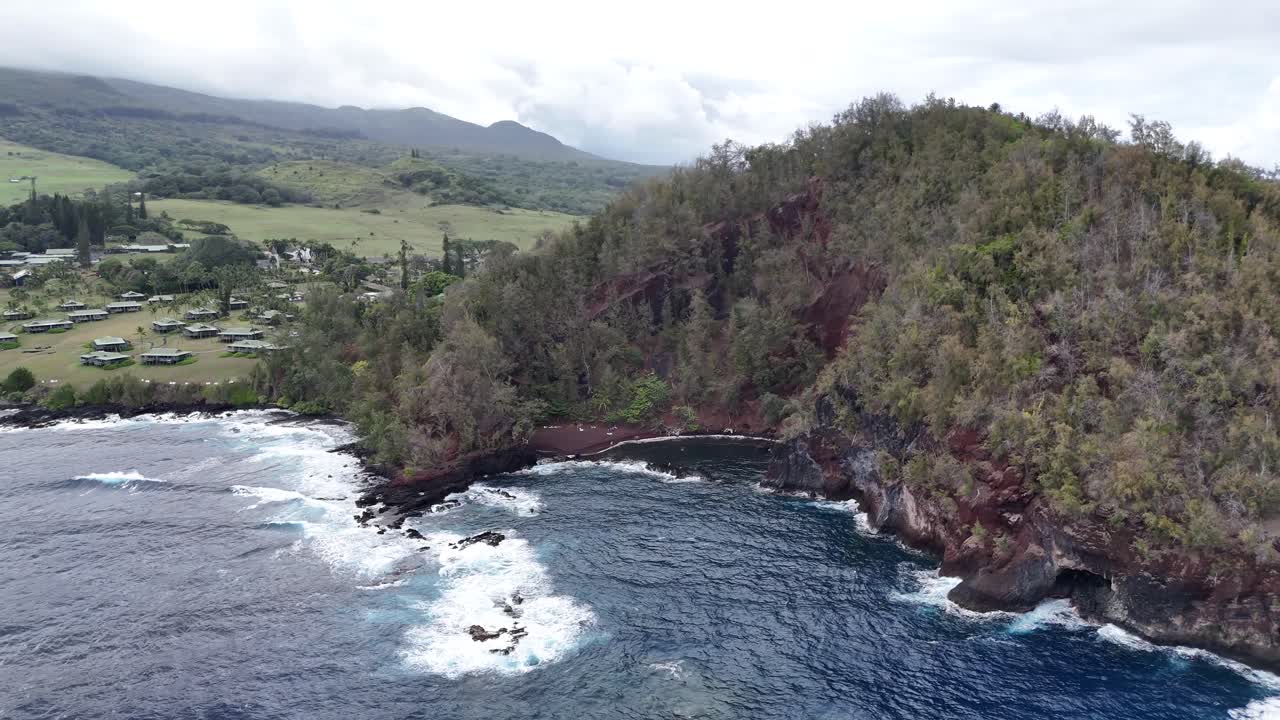 Drone view of Hana, Maui, Hawaii showing the beach, coastal village, and lush mountains. Tropical paradise with vibrant scenery, ocean waves, and island charm