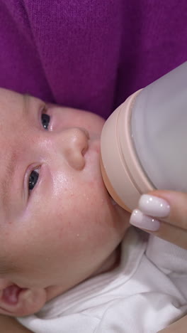 beautiful newborn boy resting in mother's hands and being fed from a bottle. little child closing eyes and gradually falling asleep. close up. vertical video