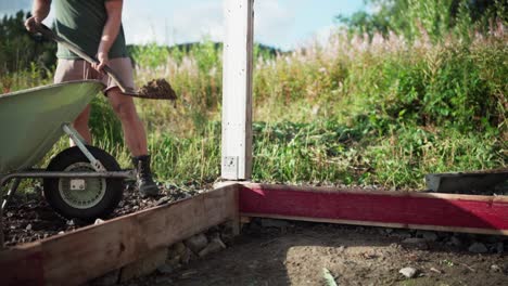 person shoveling soil from wheelbarrow in the backyard