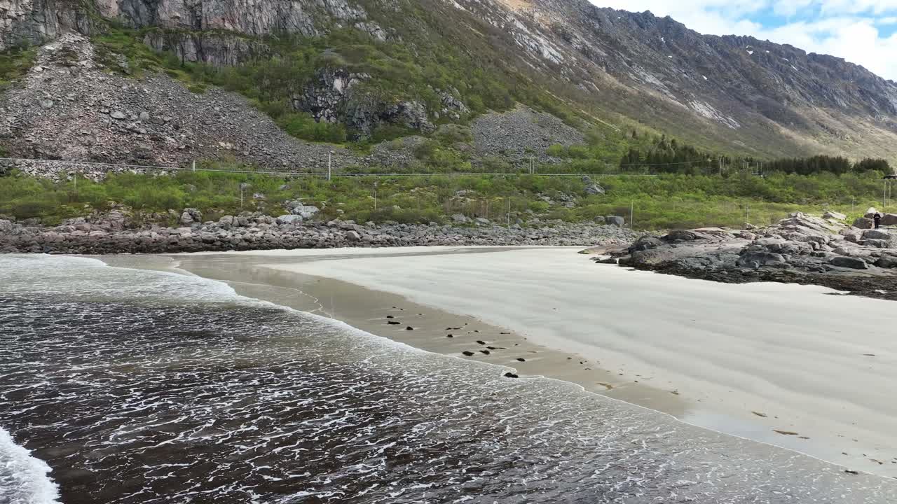 Aerial flying back over waves at Rorvik beach towards land with mountain and road in view