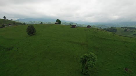 Toma-Aérea-De-Un-Pintoresco-Pueblo-Con-Casas-Dispersas-En-Medio-De-Verdes-Colinas,-Bajo-Un-Cielo-Nublado,-Durante-El-Día