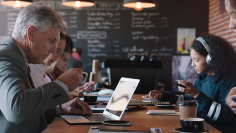 Diversos-Empresarios-Que-Trabajan-En-Una-Cafetería-Llena-De-Actividad-Bebiendo-Café-Relajándose-En-El-Almuerzo-Usando-Tecnología-En-Un-Restaurante-Concurrido