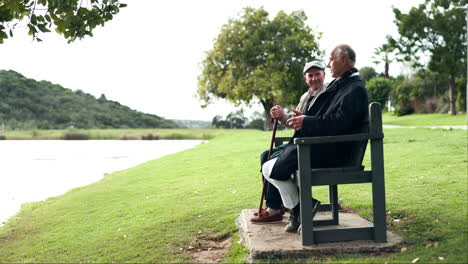 two elderly men sitting on a bench in a park by a lake