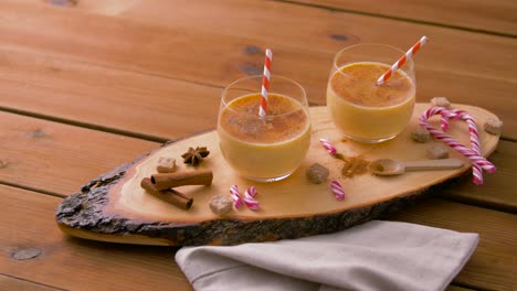 glasses of eggnog, ingredients and spices on wood.christmas, winter holidays and seasonal drinks concept – glasses with eggnog, ingredients and aromatic spices on wooden board over snow falling