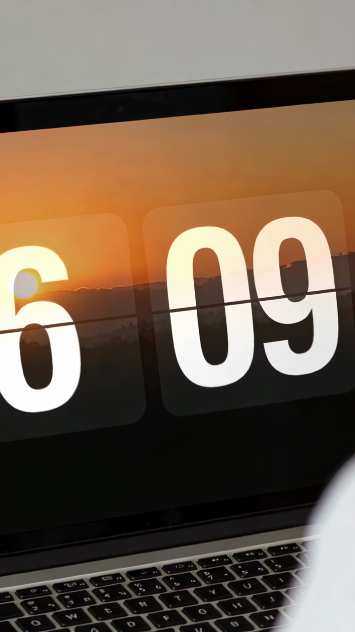Vertical video: Panning camera showing laptop clock 6:09 at desk, person in white top checking time