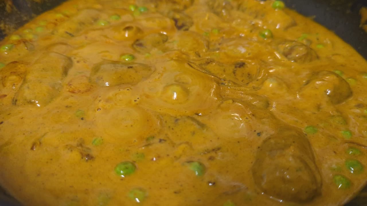 Close up, Curry on the stove boiling and bubbling in a black pot with steam.