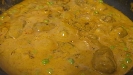 close up, curry on the stove boiling and bubbling in a black pot with steam.