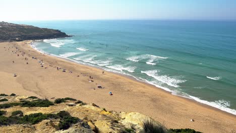 portugal, carvoeira, foz do lizandro beach from distance with surfers in the water