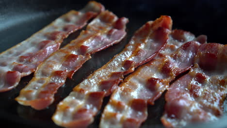 Crispy-bacon,-rich-in-fat-and-colour,-sizzling-and-smoking-in-a-hot-pan