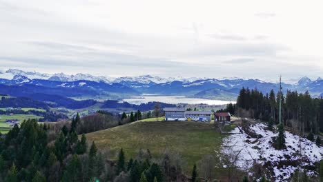 Aerial-View-nature-and-rural-remote-cabin-near-lake-Sihlsee-and-snowy-mountains,-Switzerland