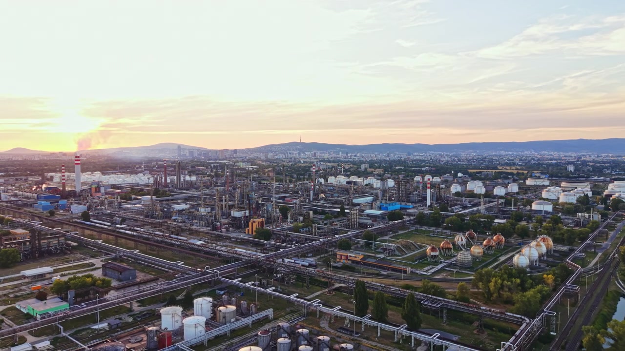 Área industrial ao pôr do sol com fábricas, tubulações e tanques de armazenamento na paisagem.
