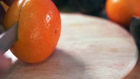 Close-Still-Shot-of-a-Hand-Grabbing-a-Clementine-and-Cutting-it-in-Half-With-a-Knife-on-a-Wooden-Surface-Then-Picking-up-Another-One