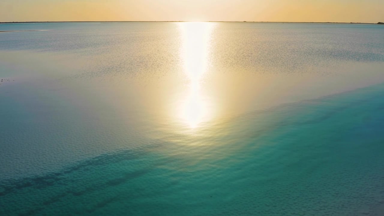 Glinting sun reflection appearing as sun nears horizon from aerial view, sweeping turquoise water