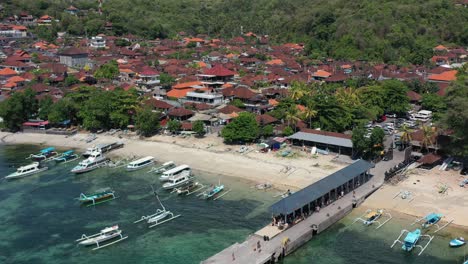 local-fishing-village-at-Padangbai-port-in-Bali-Indonesia-with-tourists-on-pier,-aerial