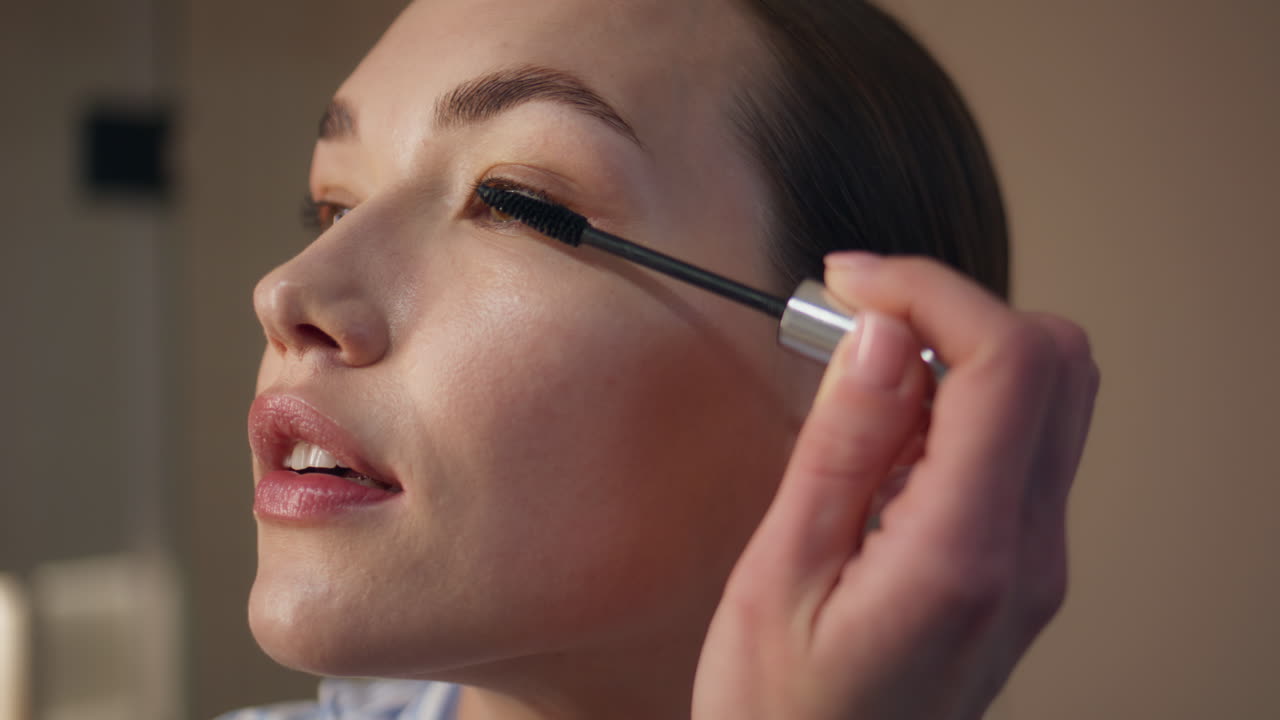 Closeup girl using mascara at home. Attractive model applying makeup in evening