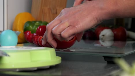 dripping wet hands cutting fresh red bell pepper on glass chopping board