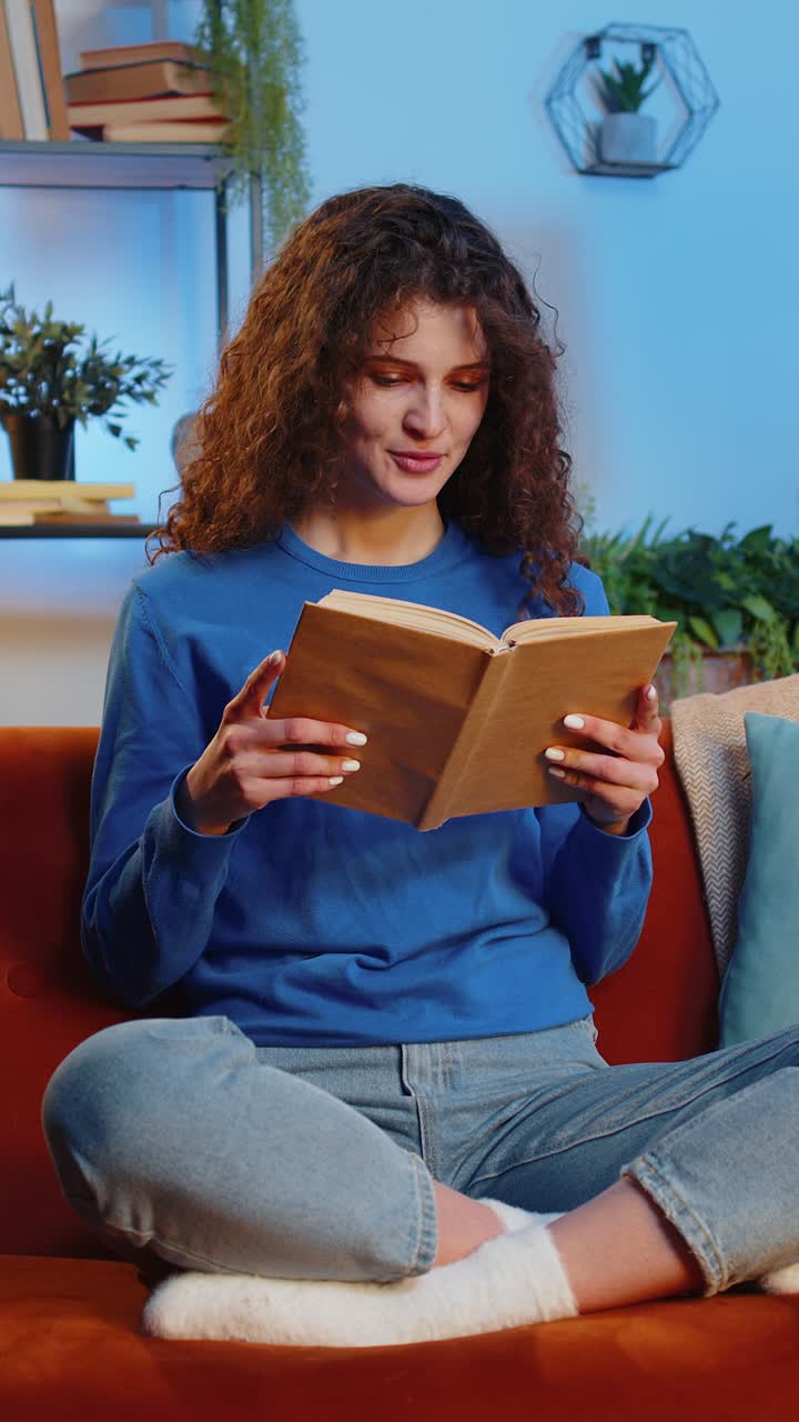 Woman reading interesting book turning pages preparing for exam sitting on couch in room at home