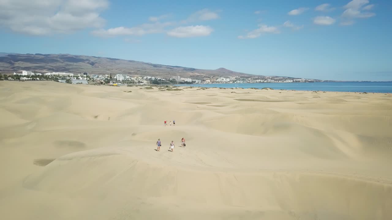 4K aerial footage of walking people in the Maspalomas sand dunes in Gran Canaria, Spain with the Atlantic Ocean in the background.