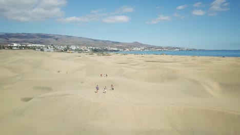 4k aerial footage of walking people in the maspalomas sand dunes in gran canaria, spain with the atlantic ocean in the background.